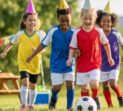 Children in party hats running with a football
